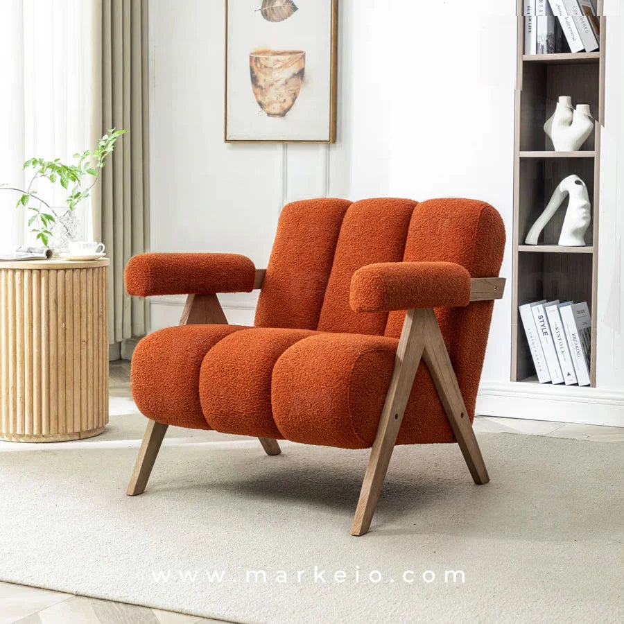 Le Fauteuil Armo bouclette rouge brique à côté d'une table d'appoint en bois.
